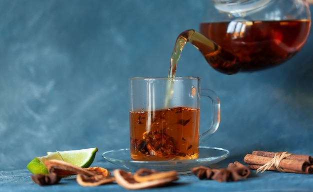 Se vierte té caliente de una tetera de vidrio en una taza