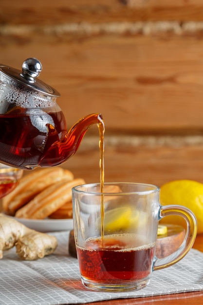Se vierte té saturado fuerte en una taza de una tetera de vidrio junto con limón y jengibre.