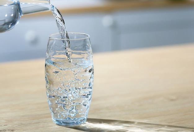 Se vierte un vaso de agua de la jarra en un solo vaso en una mesa de cocina