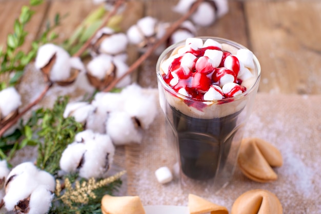 Se vierte un vaso de café y malvavisco con almíbar. galletas con los tradicionales deseos navideños. rama con algodón sobre un fondo de madera