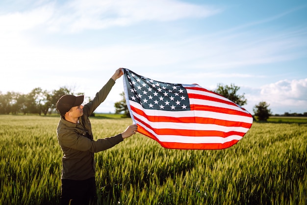 Vierter Juli. Patriotischer Mann mit der amerikanischen Nationalflagge im Feld. Junger Mann, der stolz eine amerikanische Flagge schwenkt. Tag der Unabhängigkeit.