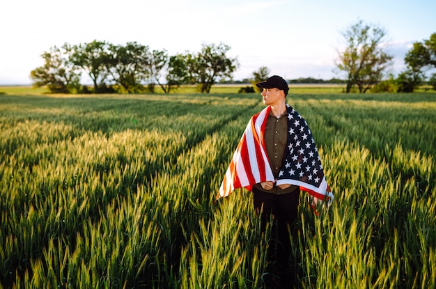 Vierter Juli. Patriotischer Mann mit der amerikanischen Nationalflagge im Feld. Junger Mann, der stolz eine amerikanische Flagge schwenkt. Tag der Unabhängigkeit.