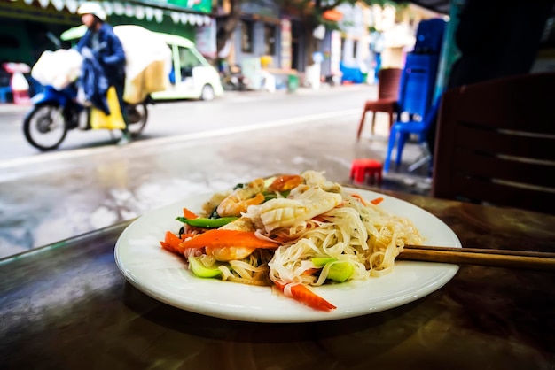 Vietnam Tailandia comida callejera asiática un plato de fideos en la mesa contra la calle asiática con motos y ciclistas