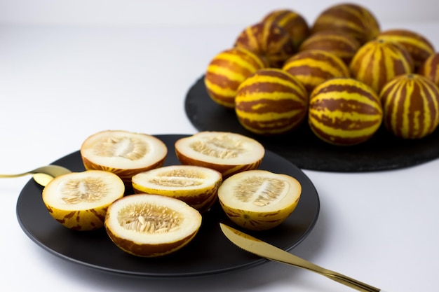 Vietnamesische Melone Nahaufnahme Ganze und geschnittene Gourmet-Miniatur-Tropenfrüchte und Messer auf einem schwarzen Teller Selektiver Fokus