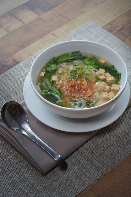 Vietnamesische Nudelschweinefleischwurstsuppe (Pho) in der weißen Schüssel auf hölzernem Hintergrund