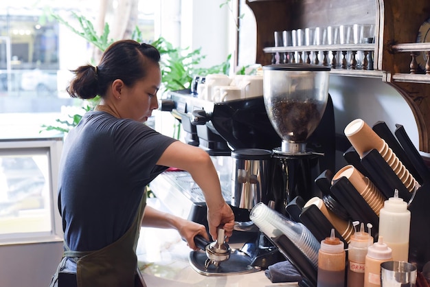 Vietnamesischer Barista presst Kaffeebohnen für eine Kaffeemaschine aus nächster Nähe