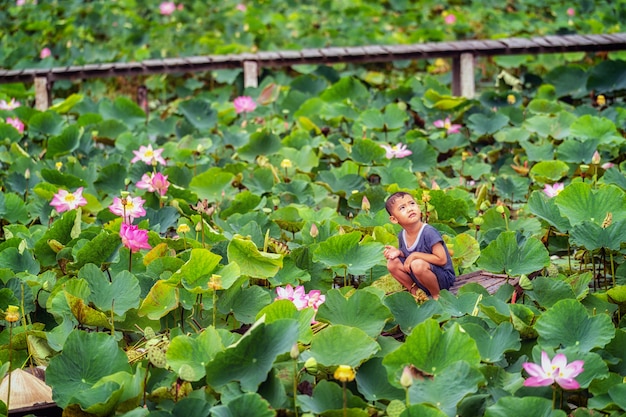 Vietnamesischer Junge, der mit dem rosa Lotos über dem traditionellen hölzernen Boot im großen Lak spielt