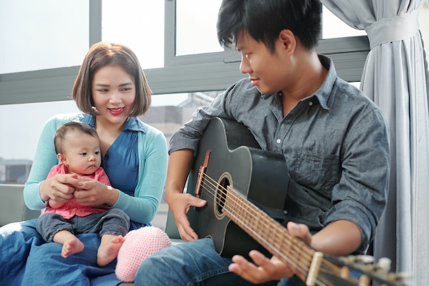 Vietnamesischer junger Mann, der Gitarre spielt und für seine kleine Tochter singt