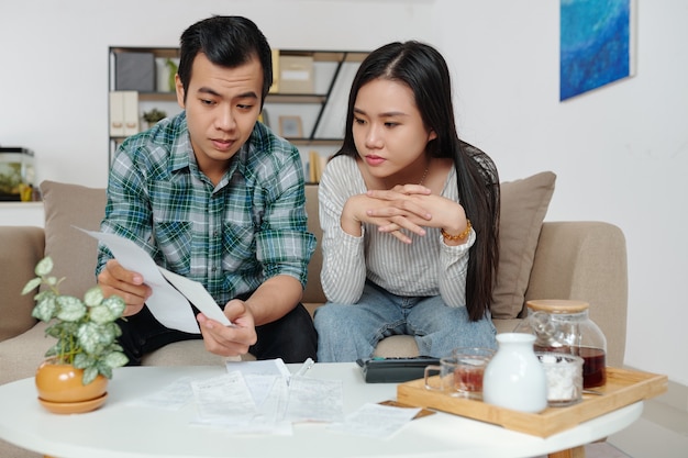 Vietnamesischer junger Mann, der seiner Freundin Rechnungen zeigt, wenn sie persönliche Ausgaben und Stromrechnungen besprechen und verwalten