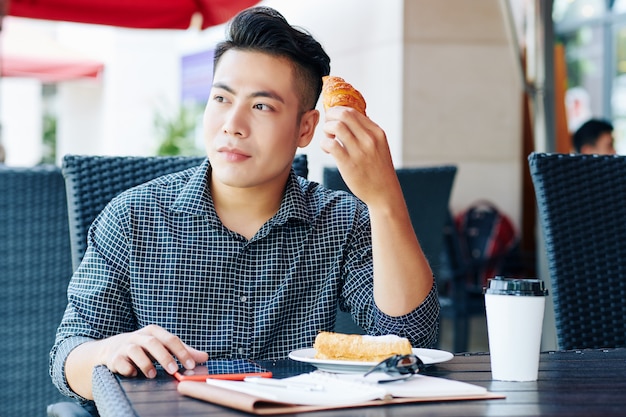 Vietnamesischer Mann, der Kaffee und Gebäck genießt