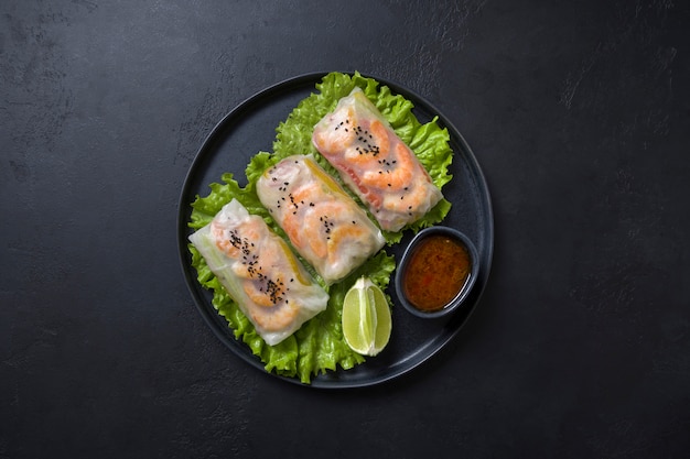 Vietnamesisches Essen Frühlingsrollen mit Gemüse, Garnelen in Reispapier auf Schwarz. Sicht von oben. Asiatische Küche.