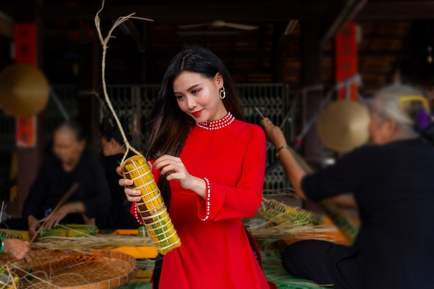 Vietnamesisches Mädchen mit Ao Dai-Kleidung sitzt in einem traditionellen vietnamesischen Haus und macht Tet-Kuchen Tet-Essen im Freien mit einer alten Frau Traditionelles vietnamesisches Neujahr Tet-Essens