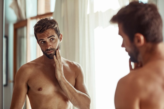 Vigilando de cerca cualquier signo de envejecimiento Foto de un hombre sin camisa mirando su piel en el espejo del baño