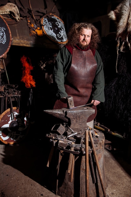 Viking forja armas e espadas na ferraria. Um homem com roupas de guerreiro está na ferraria.