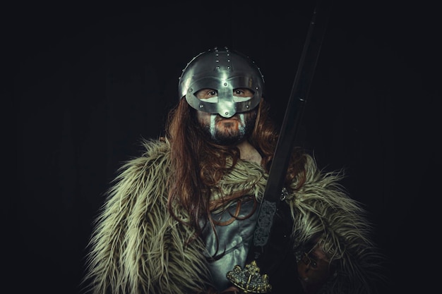 Viking, guerreiro escandinavo com pinturas de capacete e guerra, usa uma espada e uma capa de pele de animal