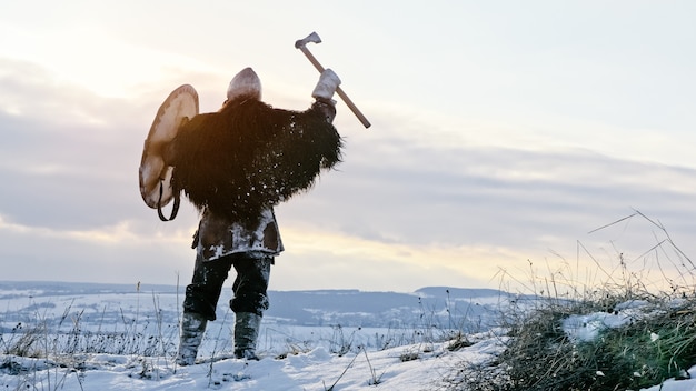 Viking medieval em armadura está gritando durante a pé no prado de inverno ao pôr do sol. reconstituição medieval.