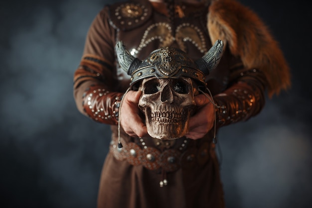 Viking vestido com roupas nórdicas tradicionais segurando um crânio humano no capacete