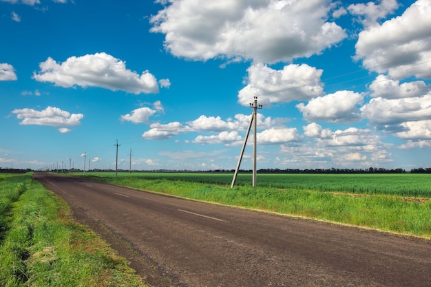 Village Road com linha de energia, campos verdes e céu azul com nuvens