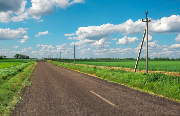 Village Road con línea eléctrica, campos verdes y cielo azul con nubes