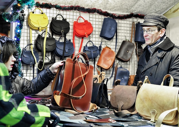 Vilnius, Lituânia - 27 de dezembro de 2015: O homem lituano oferece bolsas de couro no mercado de Natal de Vilnius. O mercado é a tradição anual e acontece de dezembro até o início de janeiro.