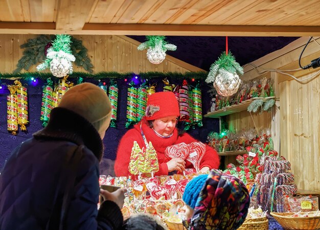 Vilnius, Lituania - 27 de diciembre de 2015: Vendedor y compradores en Stall con dulces coloridos y festivos tradicionales en el mercado de Navidad en Vilnius, Lituania.