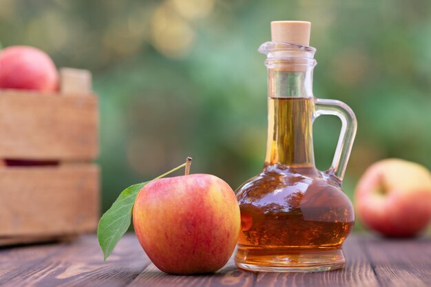 vinagre de maçã em jarra de vidro e maçãs frescas maduras na mesa de madeira ao ar livre