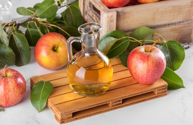 Vinagre de maçã em uma garrafa de vidro e maçãs frescas com folhas sobre fundo claro