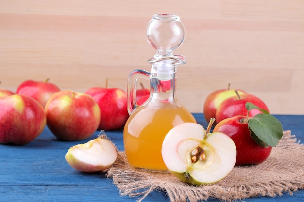 Vinagre de manzana junto a manzanas rojas frescas sobre una mesa azul sobre un fondo de madera natural