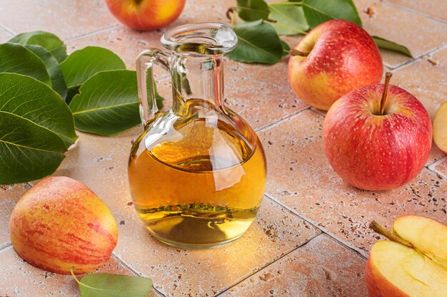 Vinagre de sidra de manzana de fruta fermentada en botella de vidrio con manzanas sobre fondo de mesa de azulejos de travertino beige