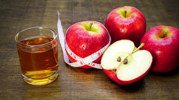 Vinagre de sidra de manzana en un vaso con manzanas y una cinta métrica sobre un fondo de madera