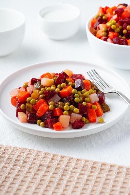 Vinagreta de ensalada rusa tradicional con verduras hervidas, pepinos encurtidos y chucrut en plato sobre mesa blanca