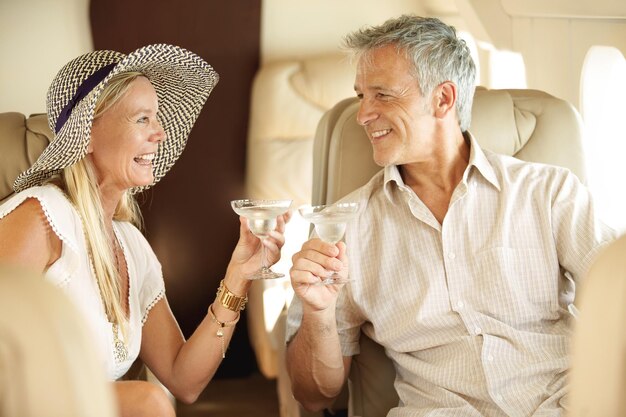 Vinculación en una escapada romántica Sonriente y feliz pareja sentada en un jet privado y brindando mutuamente