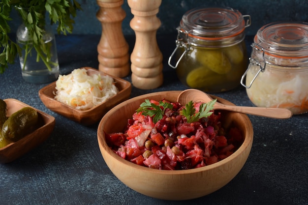 Vinegret o vinagreta. Ensalada roja tradicional rusa con verduras cocidas y en escabeche, guisantes, remolacha, en un tazón de madera sobre fondo rústico.