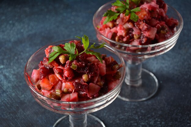 Vinegret ou vinagrete. salada russa vermelha tradicional com legumes cozidos e em conserva, ervilhas, beterraba, em duas tigelas de vidro no fundo cinza.