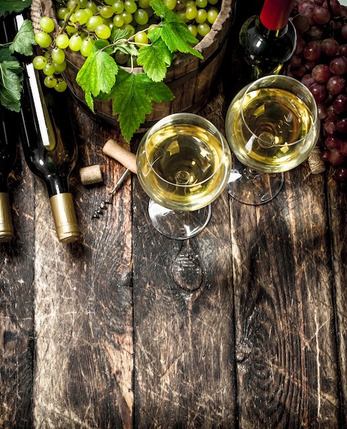 Vinho branco e tinto com ramos de uvas na mesa de madeira.