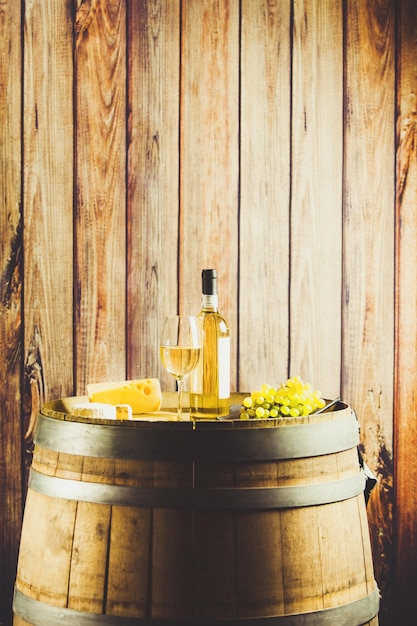 Vinho branco em garrafa de vidro de uva e queijo no fundo de madeira da frente do barril