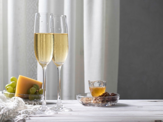 Vinho branco em taças altas e aperitivo com queijo, uvas, mel e nozes