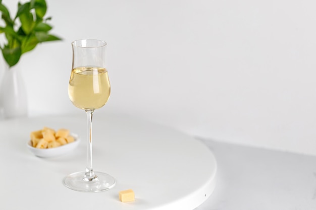 Vinho branco em vidro rico em uma mesa redonda branca com queijo e vaso de verduras Fotografia branca