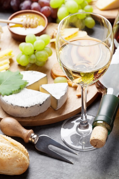 Vinho branco, uva, pão, prato de queijo e mel na mesa de pedra