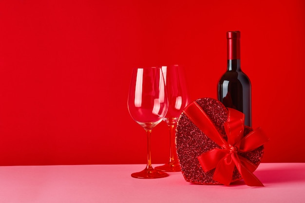 Vinho, copos e caixa de presente em forma de coração com uma fita vermelha na mesa escarlate. Conceito do dia dos namorados Foco seletivo.