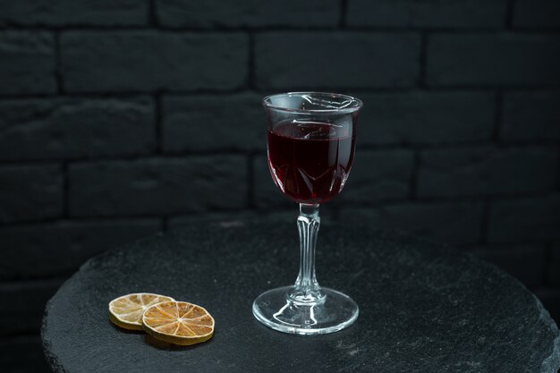 Vinho doce vermelho escuro em um copo fica sobre uma mesa de madeira preta decorada com fatias de laranjas secas em um fundo preto no restaurante. Ótima adição ao jantar