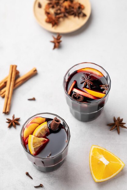 Foto vinho molled com maçã laranja e canela em copos em um fundo claro o conceito de uma bebida quente tradicional de inverno com especiarias e frutas