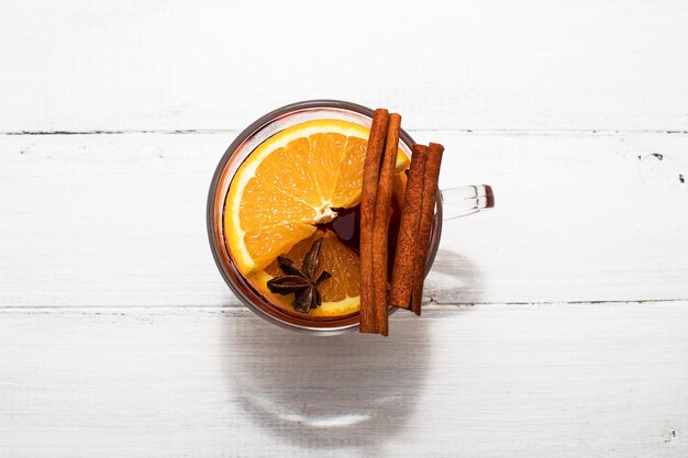 Vinho quente caseiro Vidro com fatias de laranja canela pauzinhos de alho suco de cereja em fundo de madeira branca Top vew espaço de cópia