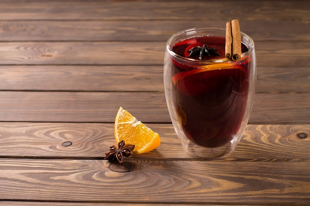 Vinho quente com canela, anis estrelado e laranja, em taça de vidro, sobre fundo de madeira