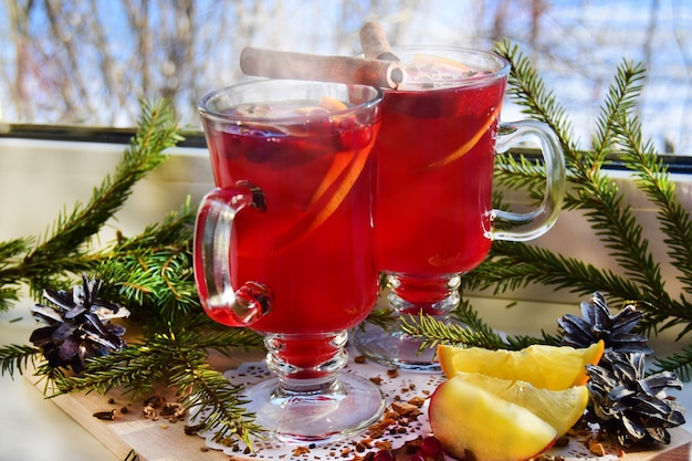 Vinho quente com especiarias e galhos de árvores de Natal em uma janela clara, lá fora é inverno. Férias de Natal e conceito de calor em casa.