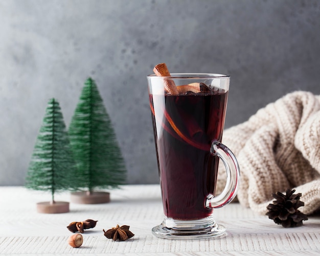 Vinho quente com especiarias em um copo com um pau de canela e árvores de natal