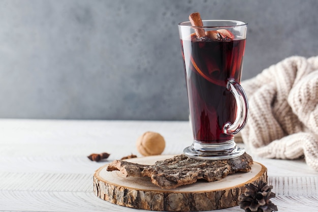 Vinho quente com um pau de canela, especiarias em um copo em um suporte de madeira com uma jaqueta de tricô na superfície