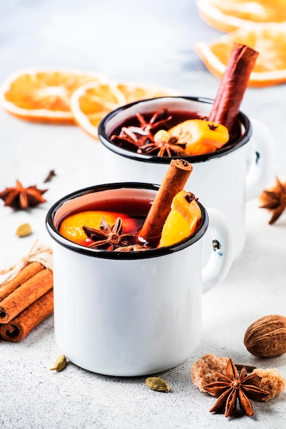 Vinho quente em canecas de metal branco com especiarias de canela e laranja na bebida tradicional de fundo de concreto nas férias de inverno Copie o espaço para texto