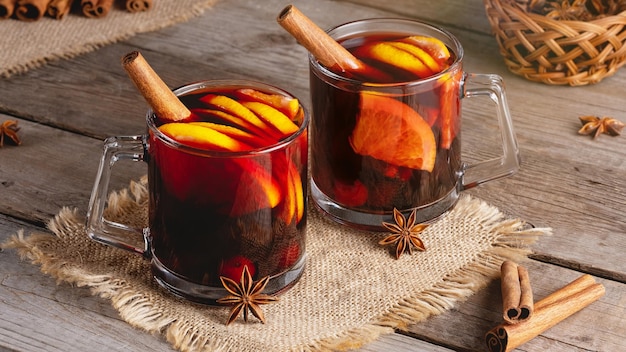 Vinho quente em canecas de vidro com especiarias e frutas cítricas em uma velha mesa de madeira