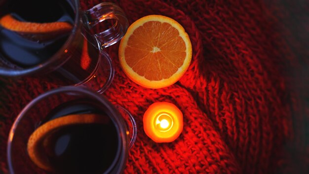 Vinho quente em canecas de vidro, vela acesa em um fundo vermelho escuro. Vinho quente vermelho com lenço laranja e vermelho